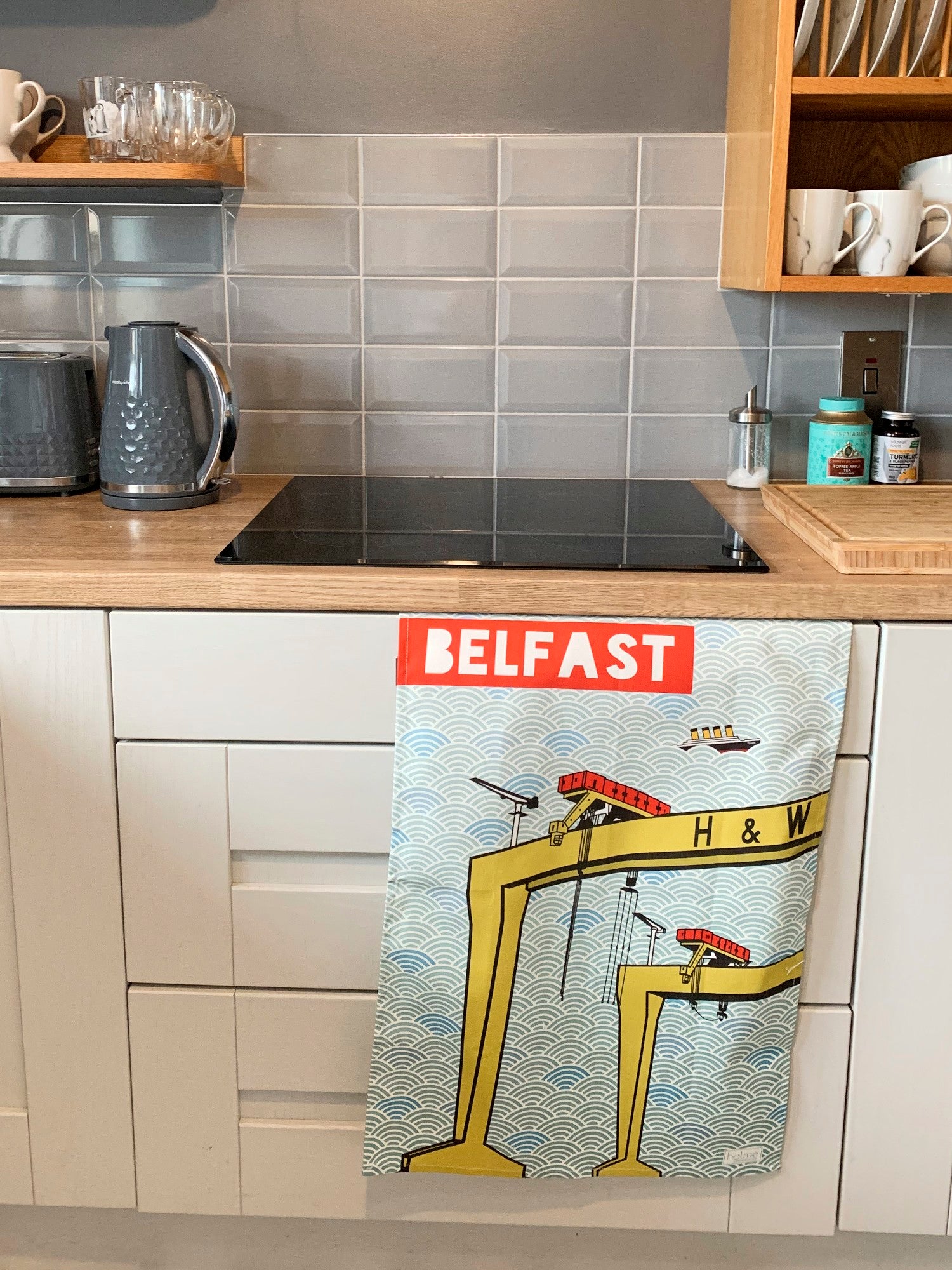 Belfast Tea Towel featuring the Harland and Wolff Cranes showing full opened product hanging from a kitchen cabinet door.
