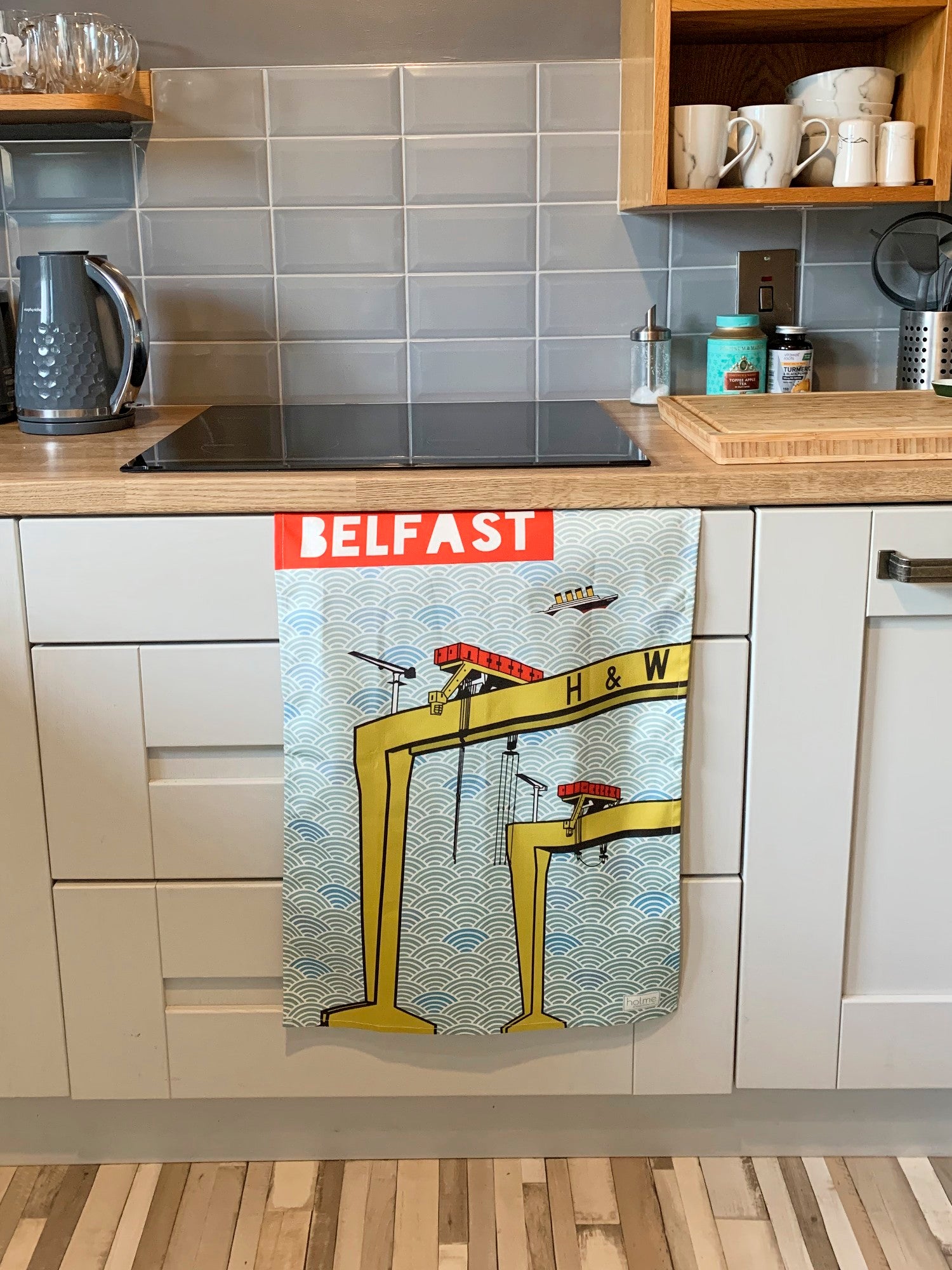 Belfast Tea Towel featuring the Harland and Wolff Cranes showing full opened product hanging from a kitchen cabinet door.